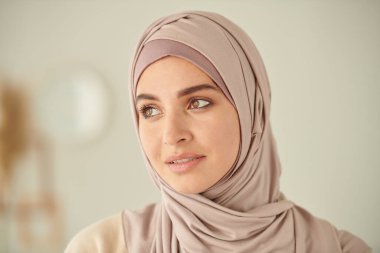 Kafasında ve omuzlarında soluk pembe tesettürlü genç Müslüman kadın portresi var.