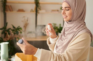 Karantina zamanında kendisine teslim edilen şeyleri dezenfekte eden tesettürlü modern Müslüman kadının yatay portresi