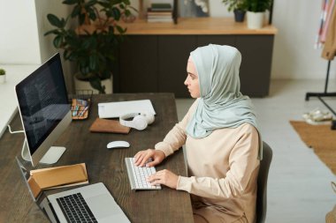 Modern Müslüman kadının masaüstü bilgisayarı kullanarak programlama üzerinde çalışmasının yatay yüksek açılı görüntüsü