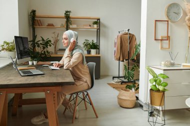 Başörtüsü ve kulaklık takan güzel, genç Müslüman kadın evde uzaktan çalışıyor, boşluğu kopyala