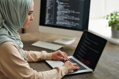Ofis masasında oturan tesettürlü profesyonel programcı dizüstü bilgisayarına bilgisayar kodu yazıyor, boşluğu kopyalıyor