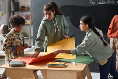 Sınıfta derste renkli kağıtlardan el işi yapan bir grup çocuk.