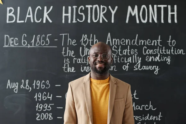 Portrait of history African American teacher smiling at camera standing against blackboard with information