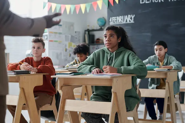 Bir grup okul çocuğu ders sırasında sıralarında oturup öğretmenlerini dinliyorlar.