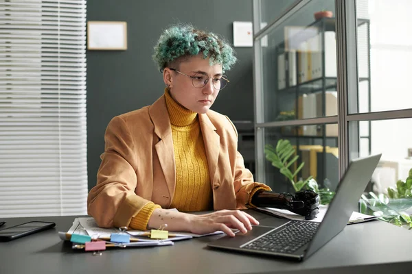 Serious businesswoman with disability concentrating on her online work on laptop in office