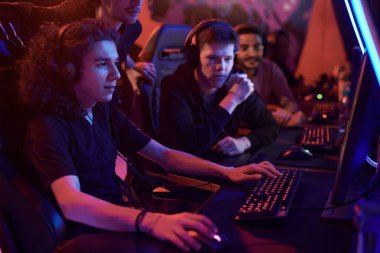 Bir grup konsantre takım üyesi bilgisayar monitörüne bakıyor ve neon ışıklı odada oyunu kazanmasına yardım ediyor.