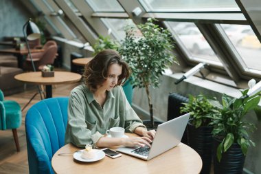 Modern kafede oturan ve cep telefonuyla arayan genç sakallı adam memnun değil.