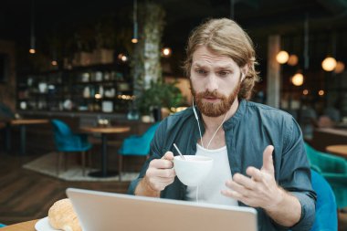 Kahve masasında oturmuş, akıllı telefondan posta okurken kahve içen sakallı yakışıklı bir adam.