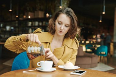 Kahve masasında oturmuş, akıllı telefondan posta okurken kahve içen sakallı yakışıklı bir adam.