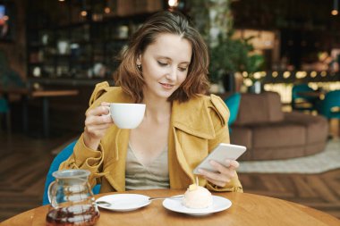 Düşünceli genç sakallı SMM yöneticisi kahve içiyor ve kafede çalışırken müşterilerin mesajlarını düşünüyor.