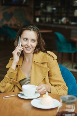 Kafedeki akıllı telefonları kontrol ederken günlük gömlekli, kahve içen ve kruvasan yiyen konsantre genç adam.