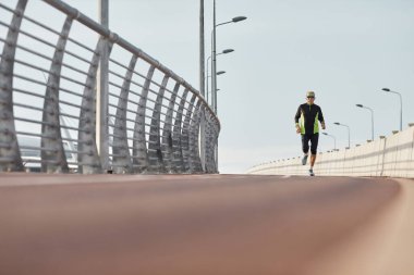 Yaşlı bir adamın modern eşofman giyerek raylarda koşarken çekilmiş yatay bir görüntüsü.