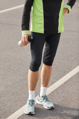 Eşofman giyen, bir şişe suyla raylarda duran, tanınmayan fit bir adamın alt vücut çekimi.