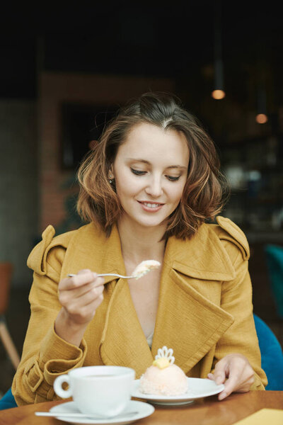 Молодой бородатый менеджер сидит за столом с чашкой кофе и круассаном и записывает голосовое сообщение для коллеги, используя смартфон в кафе