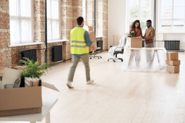 Yeni alandaki polietilen altındaki eşyaları yerleştiren ofis sahiplerine kutu taşıyan yükleyici