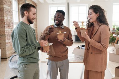 Bir grup pozitif, genç, ırklar arası girişim sahibi şirket sahibi kutular dolusu yeni ofiste öğle yemeği molası verirken çember oluşturup sohbet ediyorlar.