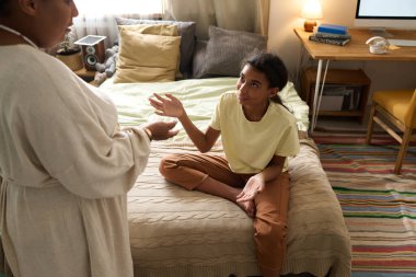 Afrikalı Amerikalı anne, genç kızıyla odasında sohbet ediyor.