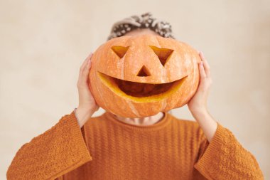 Kahverengi kazaklı, tanınmayan bir kadın Cadılar Bayramı partisine karşı komik bir balkabağı tutuyor.