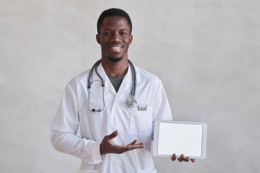 Dijital tablet ekranı gösteren beyaz önlüklü modern yetişkin doktorun orta stüdyo portresi.