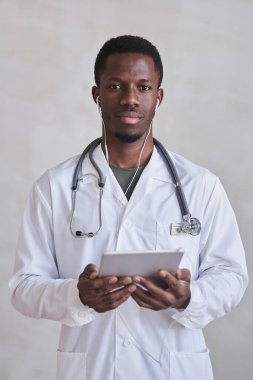 Elinde dijital tabletle kameraya bakan kulaklık takan yakışıklı yetişkin doktorun dikey portresi.