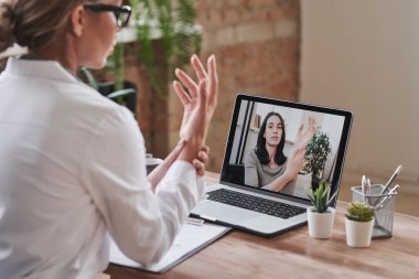 Beyaz önlüklü modern bir doktor çatı katında masa başında oturmuş kamerada bilek eklemine dokunuyor.