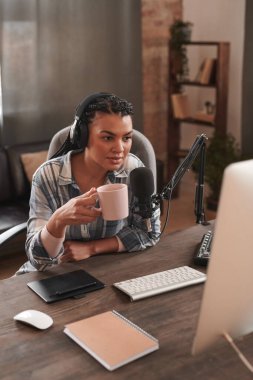 Saçları örgü örgülü, tavan arasında oturmuş blog yazıp kahve içen şık bir genç kadının dikey yüksek açılı portresi.