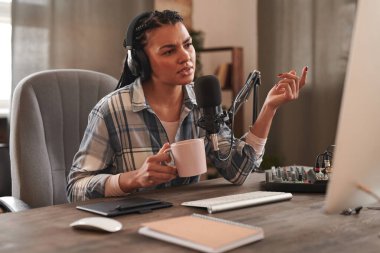 Modern kadın etkisinin yatay portresi. Masaüstü bilgisayarının önündeki tahta masada oturmuş elinde kahve fincanı tutarak ciddi sorunlar hakkında konuşuyor.