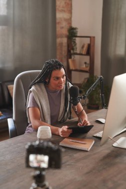 Modern bir genç kadının gündelik kıyafetlerini giyerken tavan arasında otururken, blog için içerik oluştururken grafik bloknot kullanırken dikey yüksek açılı görüntüsü.