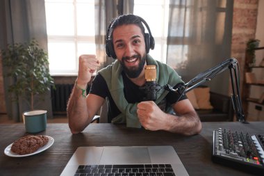 Orta yatay, neşeli sakallı Orta Doğulu, sıradan giysiler giyen, masada tek başına oturan ve eğlenen