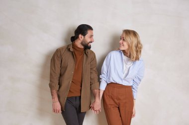 Duvara yaslanıp el ele tutuşan ve flört eden sevimli genç bir çiftin orta boy portresi.