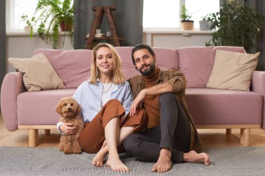 Güzel genç bir çiftin portresi kanepede oturuyor ve küçük köpekleri kameraya bakıyor, boşluğu kopyalıyor.
