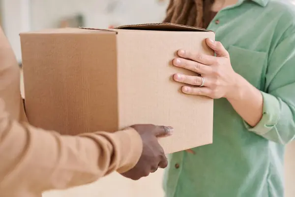 Close-up of unrecognizable woman in green shirt taking delivery of box from black man