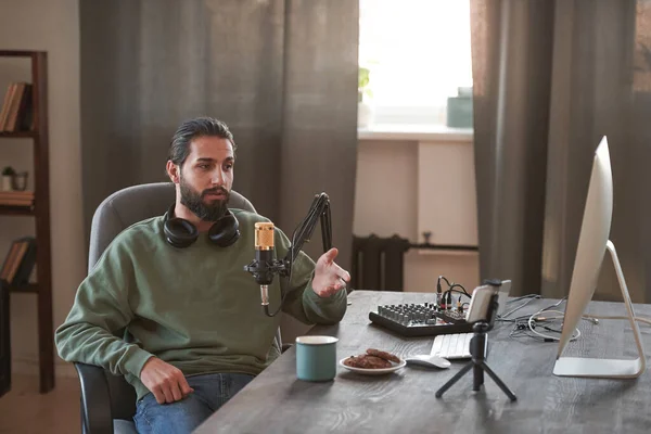 stock image Portrait of young Middle Eastern influencer sitting relaxed at desk in loft room creating content for blog looking at smartphone camera