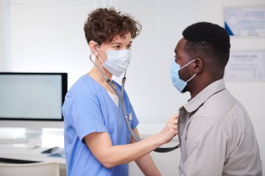 Steteskop kullanarak Afrika kökenli Amerikalı hastaları inceleyen profesyonel tıp işçilerinin orta boy portresi.