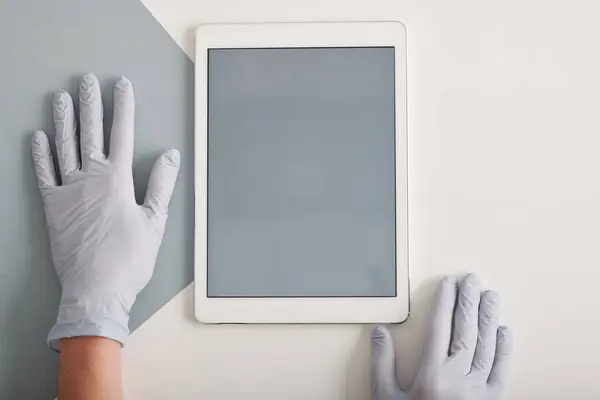 Conceptual top-down flat lay shot of hands in protective latex gloves and digital tablet with gray screen on table, copy space