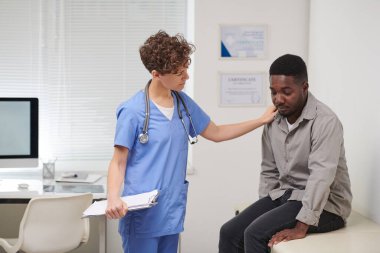 Uzman kadın doktorların üzgün Afrikalı Amerikalı erkek hastaları rahatlatırken orta ölçekli bir pozu.