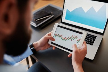 Tanınmayan bir adamın yüksek açılı görüntüsü. Hisse senedi alım satımında çalışıyor. Haritaları ve grafikleri izliyor.