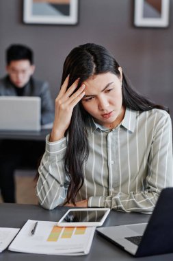 Genç Asyalı kadının dikey portresi ofiste zor veriler üzerinde çalışırken başını ovuşturuyor.