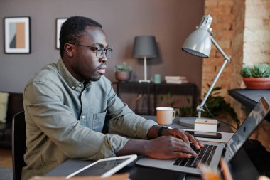 Modern siyahi adamın masanda oturmuş dizüstü bilgisayardaki istatistiklerle çalışırken çekilmiş yatay bir fotoğrafı.