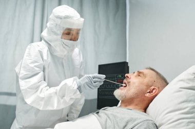 Koruyucu kıyafet giyen modern doktor acil serviste yetişkin bir hasta için PCR testi yapıyor.