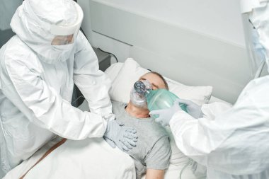 Yüksek açılı, tanınmayan doktorların koruyucu giysiler giyip olgun bir adamın kalp masajı yapmasını gösteren görüntüleri.