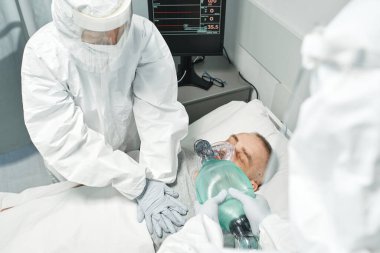 Tanınmayan tıbbi işçilerin kişisel koruma ekipmanları takıp olgun bir adama suni teneffüs yaparken yüksek açılı görüntüsü.