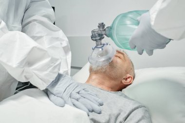 Tanımlanamayan profesyonel tıp çalışanları kişisel koruma ekipmanları giyip olgun bir adama suni teneffüs yapıyorlar.