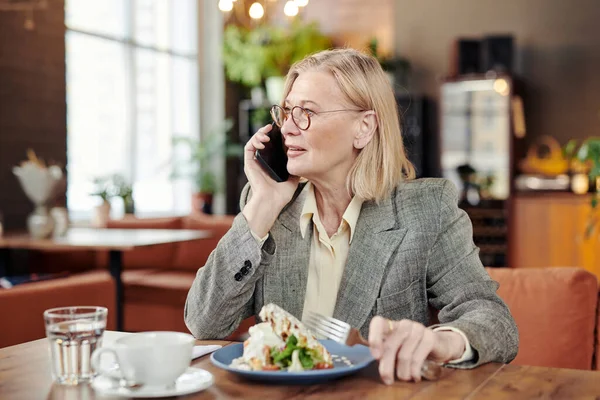 Mature businesswoman talking on mobile phone at the table while having lunch at the restaurant