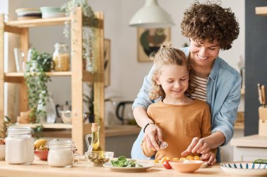 Mutlu genç anne oğluna mutfakta birlikte yemek pişirirken salata için sebze kesmeyi öğretiyor.