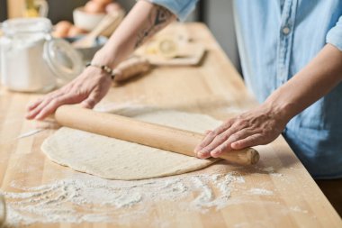 Masadaki ev yapımı fırın için merdaneli hamuru yuvarlayan genç bir kadının yakın çekimi.