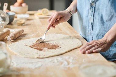 Ev hanımının mutfakta çörek pişirmek için kaşıkla tarçın ve hamur eklediği yakın plan.