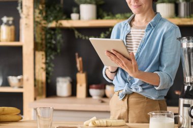 Mutfakta yemek pişirirken yemek tarifini okumak için tablet kullanan genç bir kadın.