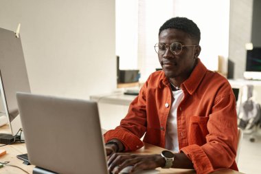 Bilgi çözerken veya yeni web sitesi oluştururken laptop ekranına bakan genç Afrikalı Amerikalı bilişim mühendisi veya web tasarımcısı
