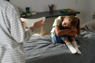 Üzgün küçük bir kız, yatakta oturup annesini dinlerken kötü davranışları hakkında konuşuyor.